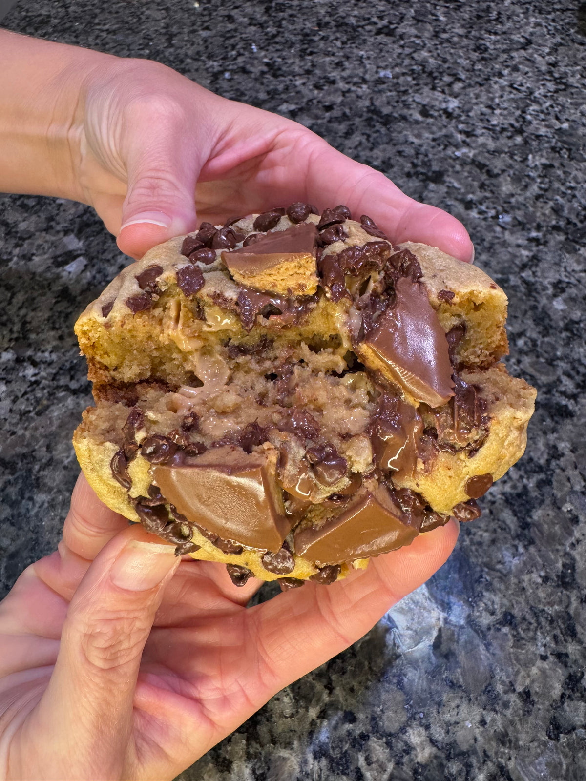 Two hands pulling apart a chocolate-studded cookie to reveal a gooey chocolate center.