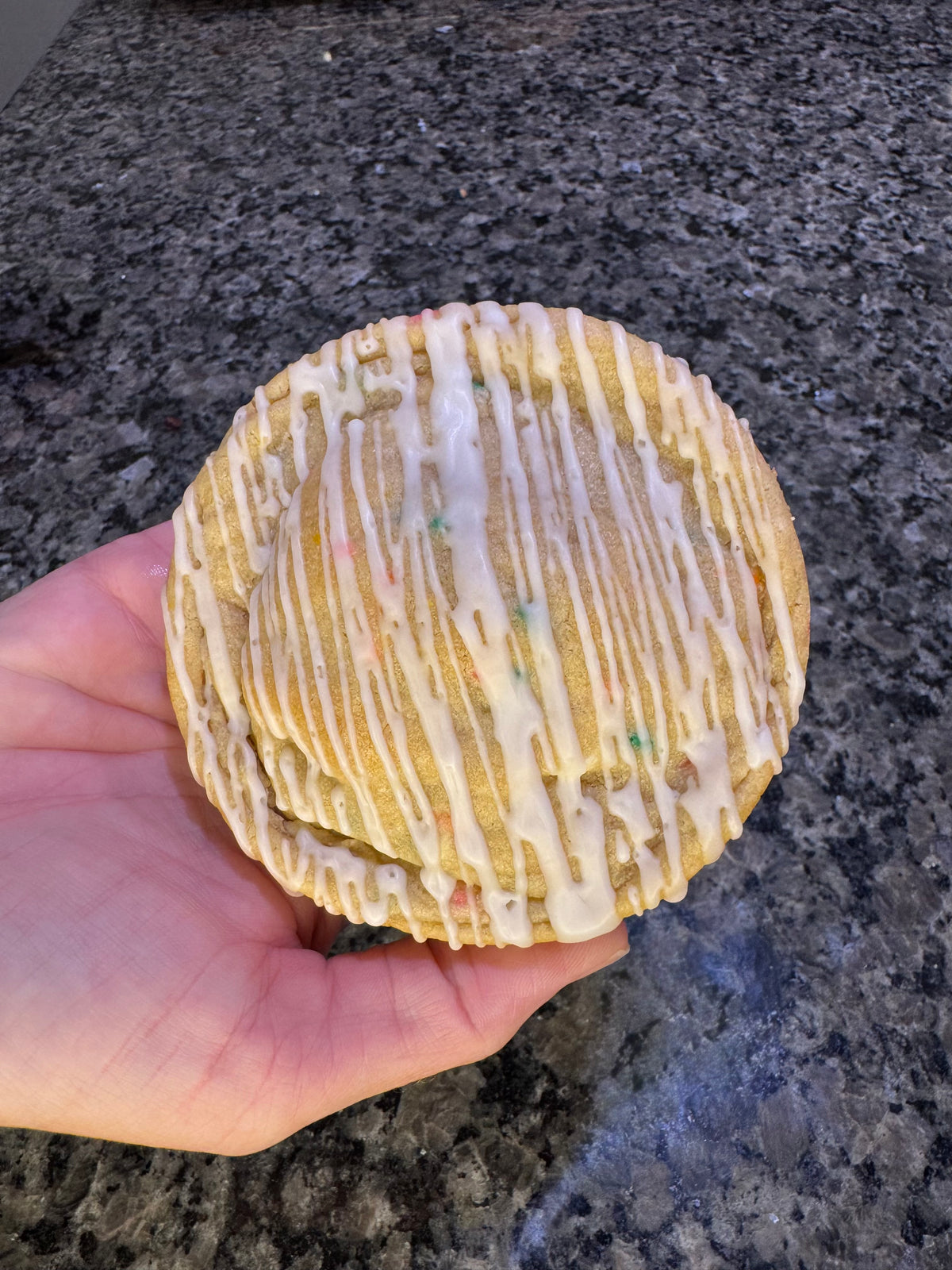 Oversized cookie topped with white icing drizzle, held in one hand.