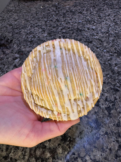 Oversized cookie topped with white icing drizzle, held in one hand.