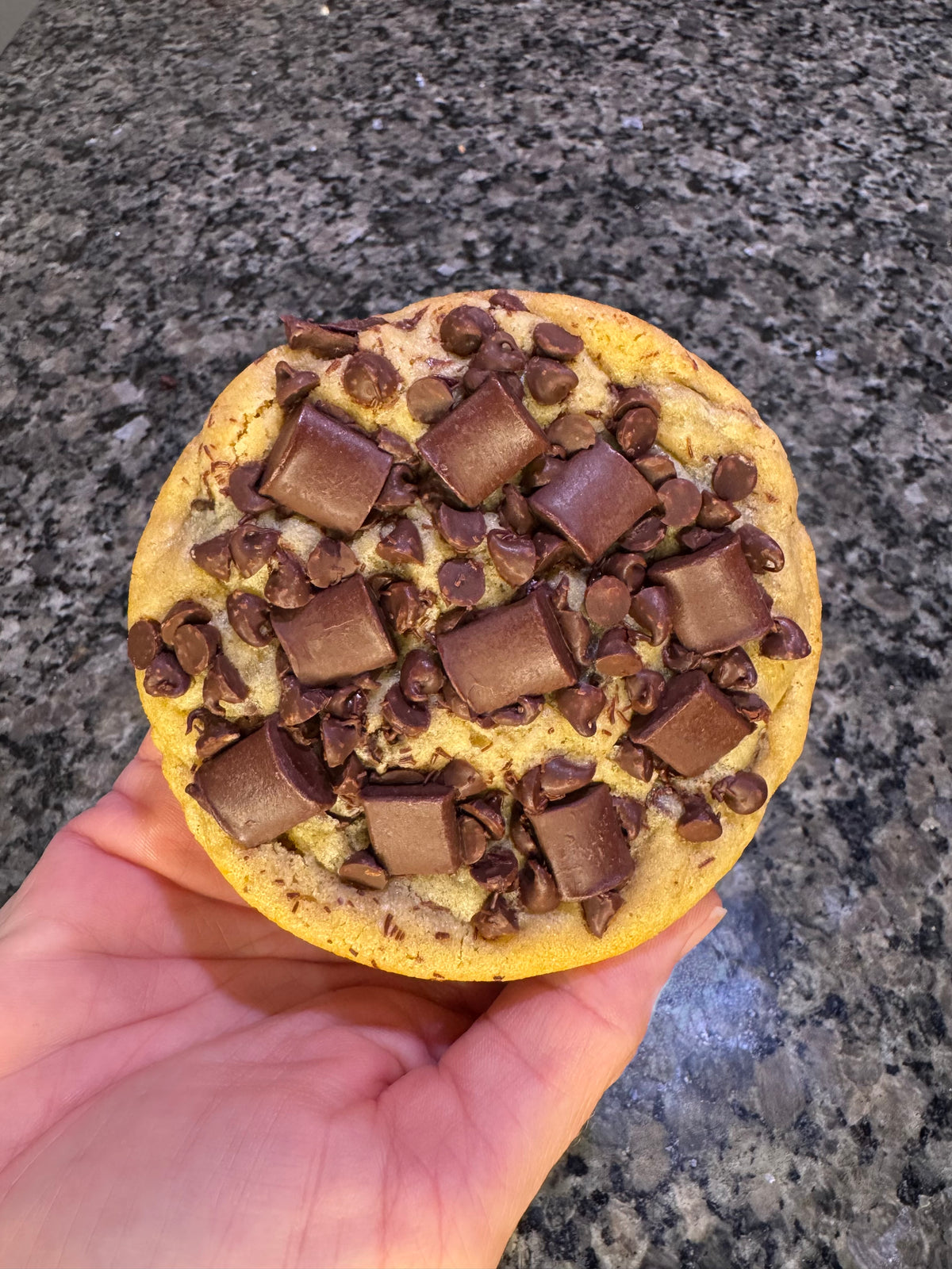 Oversized cookie topped with milk chocolate chunks and chocolate chips, held in one hand.