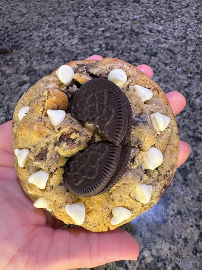 Oversized cookie topped with chocolate sandwich cookies and white chips, held in one hand.