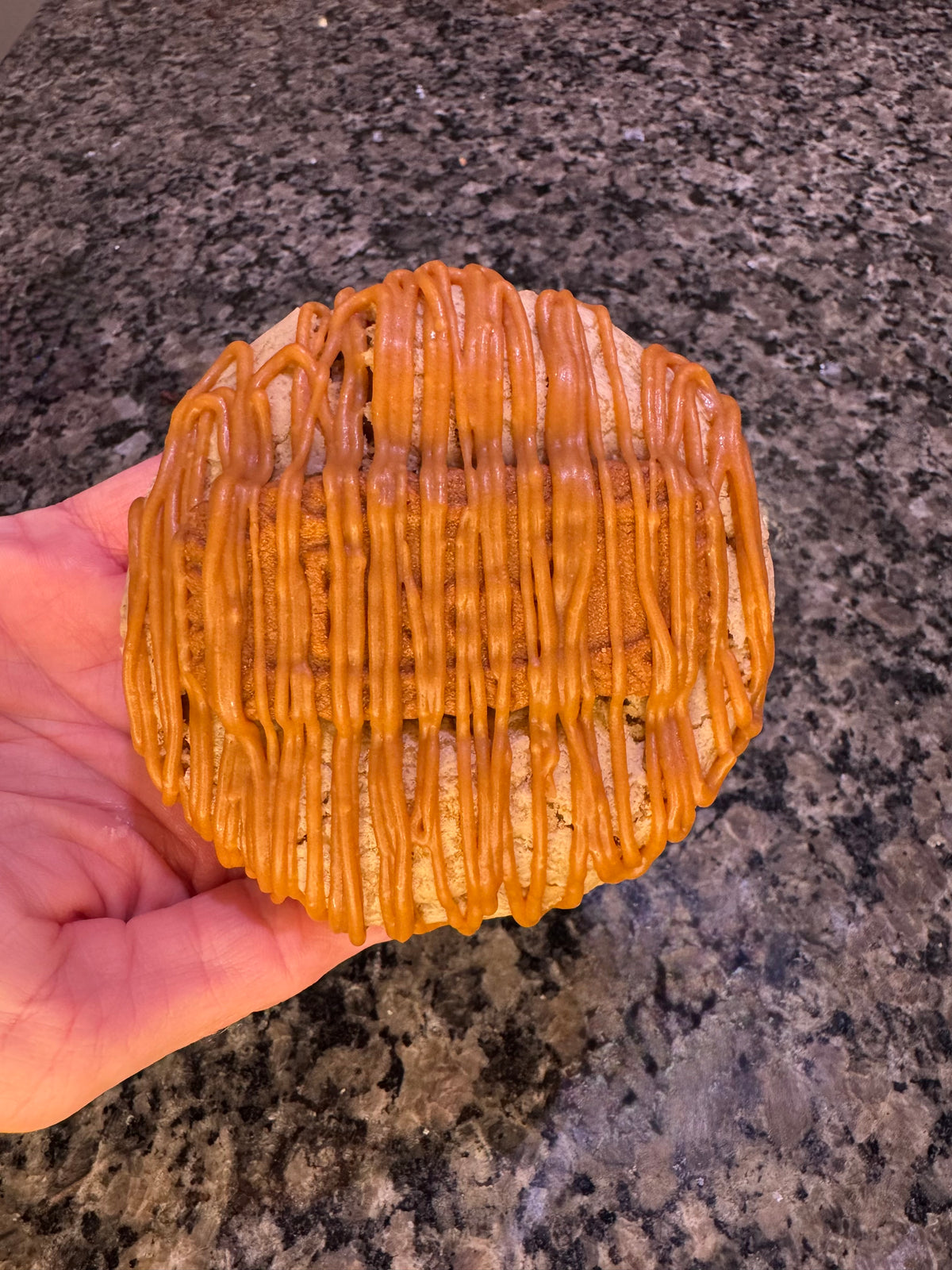 Oversized cookie covered with a caramel-colored drizzle, held in one hand.