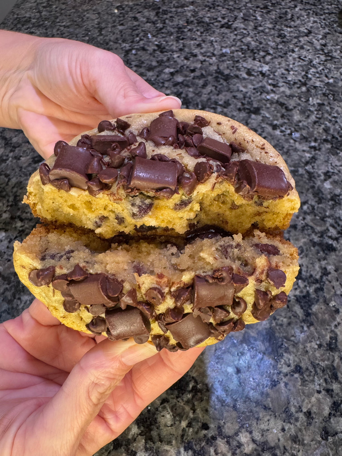 Large chocolate-studded cookie split open and stacked to show its thick, soft center.