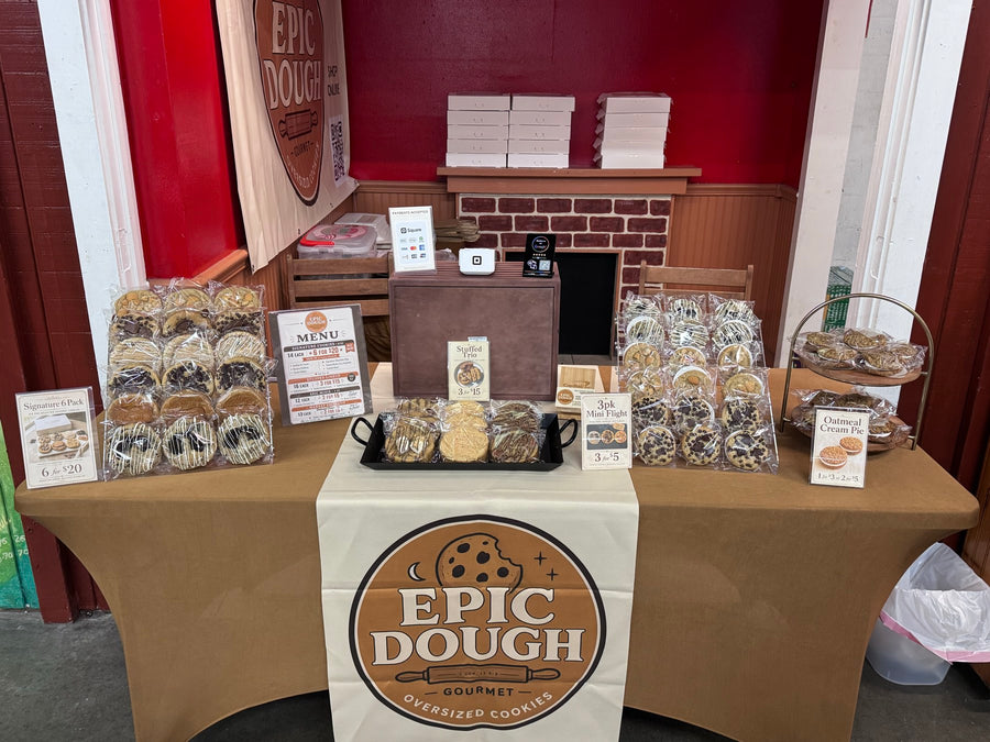 The Epic Dough market table, with packaged cookies, a tiered stand and printed menu cards.