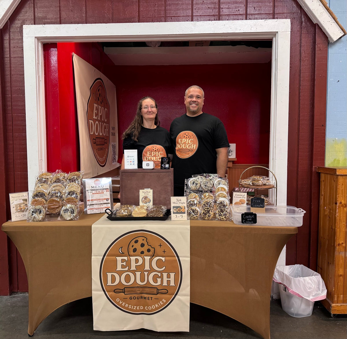 The Epic Dough market booth, with two people standing behind a table of packaged cookies under an Epic Dough banner.
